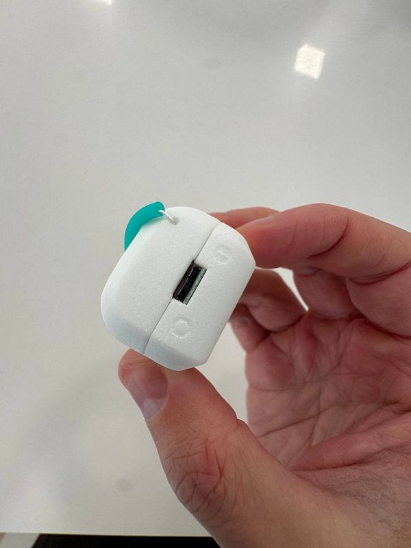 A person is holding a small, white device with a USB port and a teal attachment.