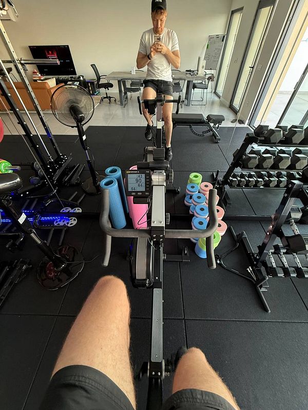 A person is exercising on a rowing machine in a well-equipped home gym.