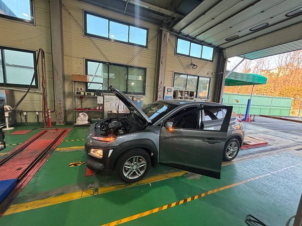 A silver Volkswagen Polo car parked in a garage with a metal shelf and some motor oil containers nearby.