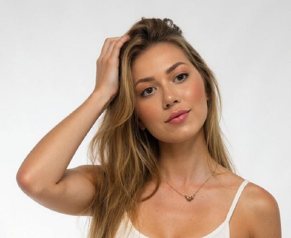 A young woman with long, wavy hair poses thoughtfully while touching her hair.