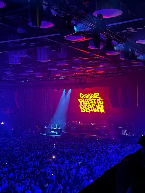 A vibrant concert scene featuring a large crowd and a prominent stage display for the Gorillaz.
