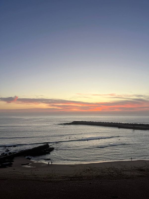 A serene beach scene at sunset with gentle waves and silhouettes of people walking along the shore.
