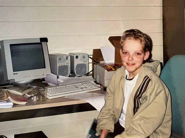 A black and white old photograph of a man standing on rocky terrain with a forested area in the background.