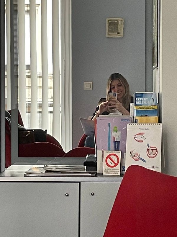 A woman is taking a selfie in a dentist's waiting room, surrounded by dental materials and a modern interior.