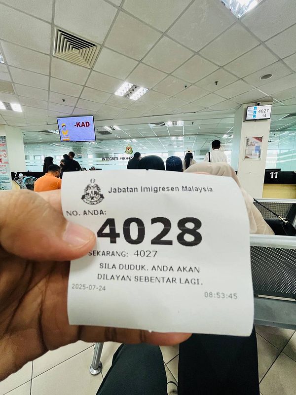 A person is holding a queue ticket at a Malaysian immigration office.