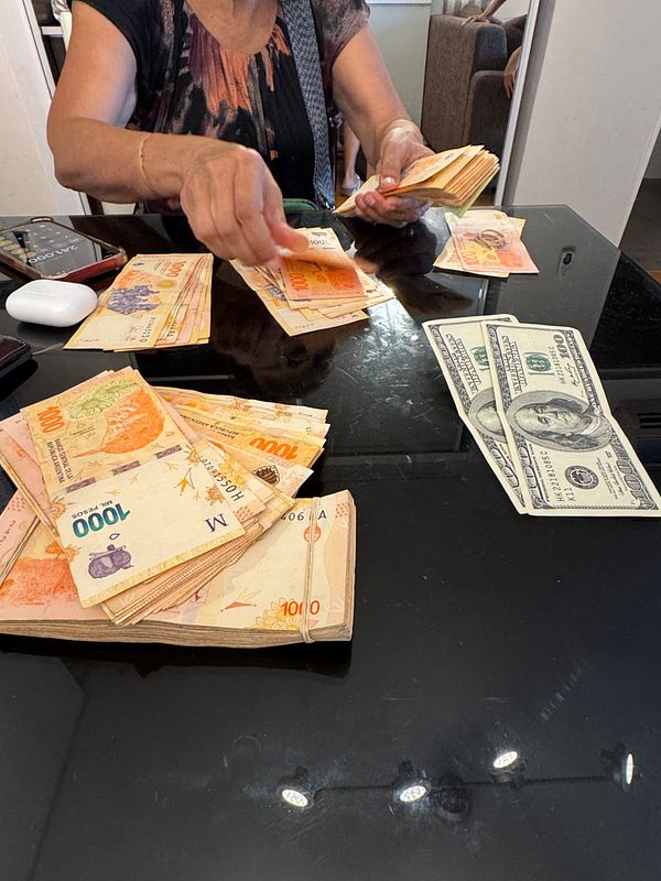A person is counting a large amount of Argentine currency on a table.