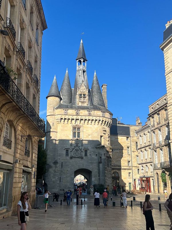 A historic stone tower with spires stands at the end of a bustling street in Bordeaux, France.