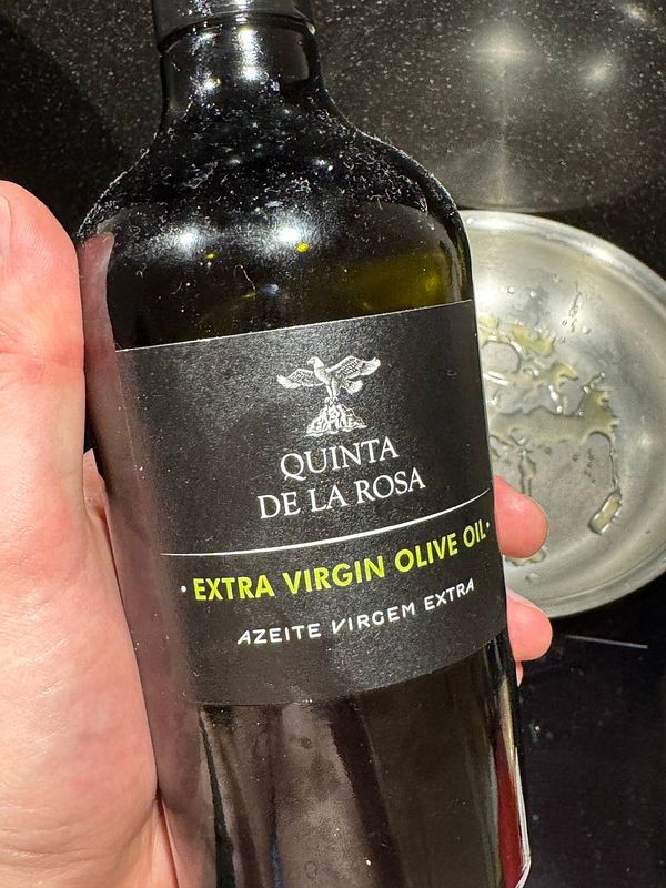 A hand holds a bottle of extra virgin olive oil in a kitchen setting.