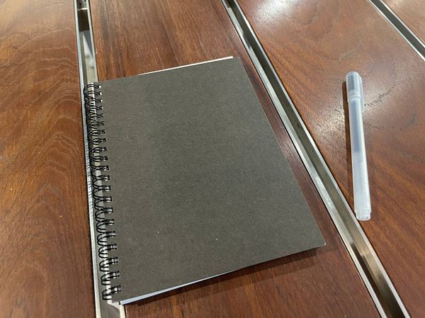A dark-colored spiral notebook and a pen are placed on a wooden table.