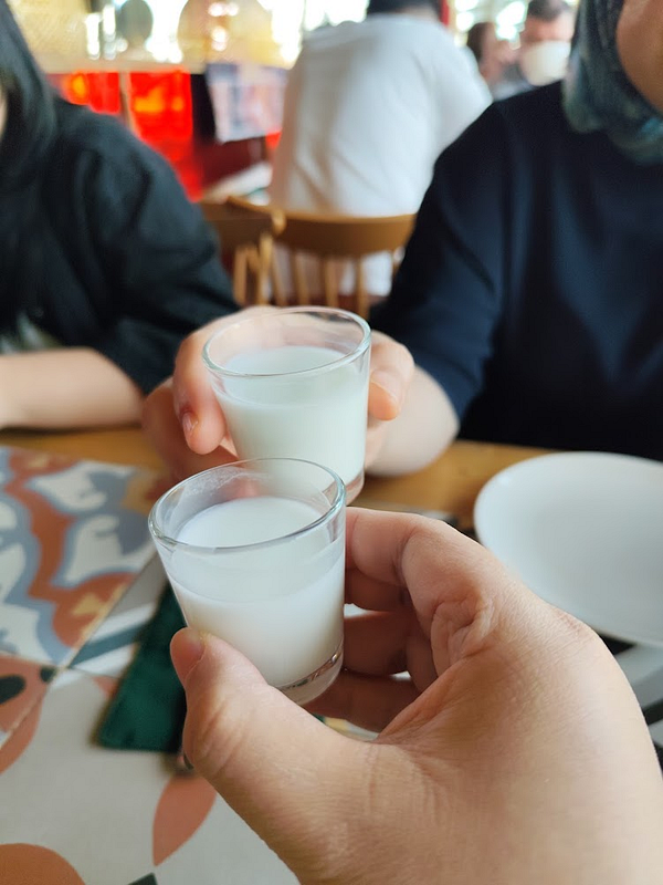 Two people clinking shot glasses filled with a white liquid during a family outing at a restaurant.