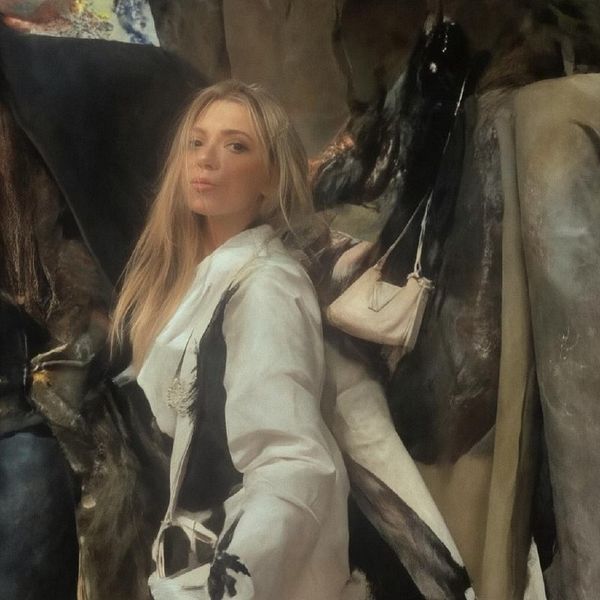 A woman poses in front of a horse, showcasing a stylish outfit.