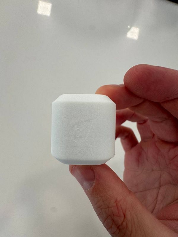 A person is holding a small, white, cube-shaped device in their hand.