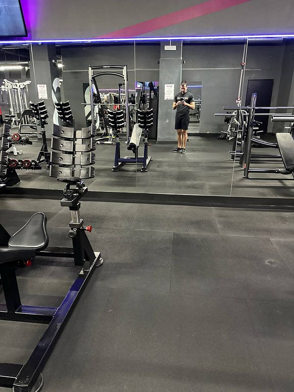 A gym interior featuring various workout equipment and a person standing in front of a mirror.