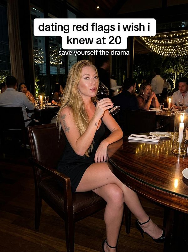A woman in a black dress sits at a restaurant table, holding a glass of wine, with text overlay discussing dating red flags.