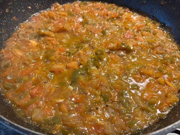 A close-up view of a simmering chicken stew in a frying pan.