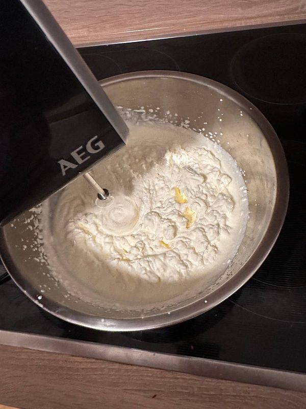 A hand mixer is blending cream in a stainless steel bowl on a kitchen countertop.