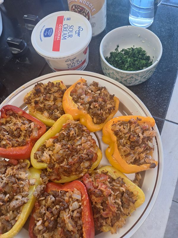 A plate of colorful stuffed peppers accompanied by sour cream and chopped herbs.