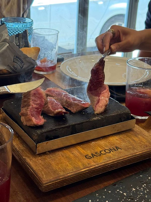 A plate of Picaña steak is being served on a hot stone with drinks in the background.