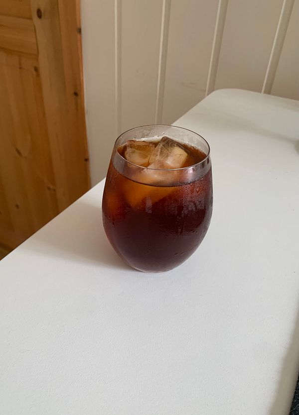 A glass of cold brew coffee with ice sits on a white surface.