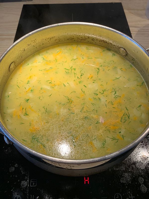 A pot of chicken soup with rice is simmering on a stovetop.
