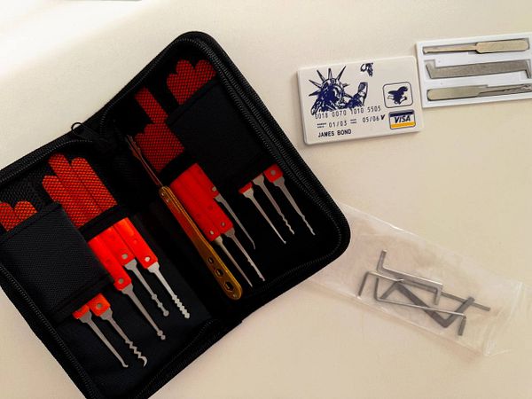 A lockpicking set with various tools is shown next to a novelty credit card and a small packet of additional metal tools on a light surface.