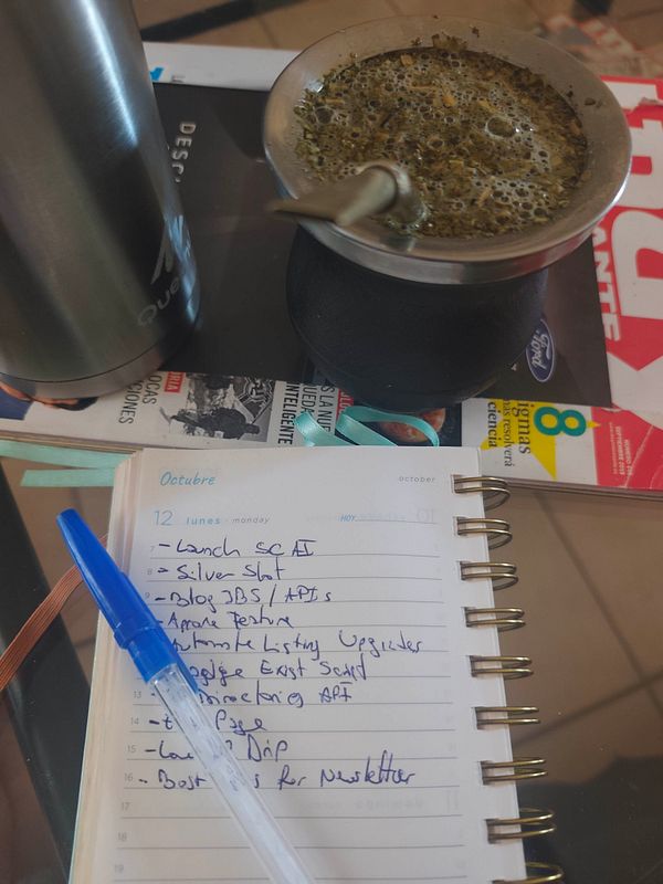 A workspace setup with a traditional mate cup filled with yerba mate, a stainless steel thermos, and a spiral-bound planner with a pen and handwritten to-do list for Monday, October 12.