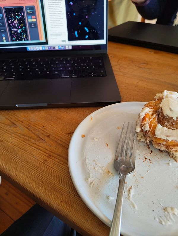 A laptop displaying interface designs sits next to a partially eaten dessert on a wooden table.