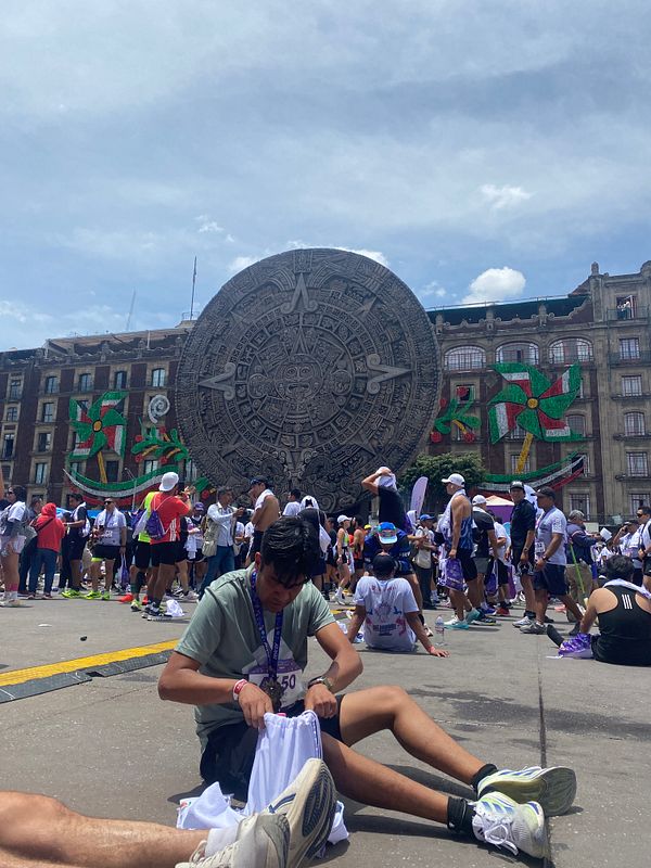 A bustling scene at the Mexico City marathon featuring a large Aztec calendar stone and numerous participants.