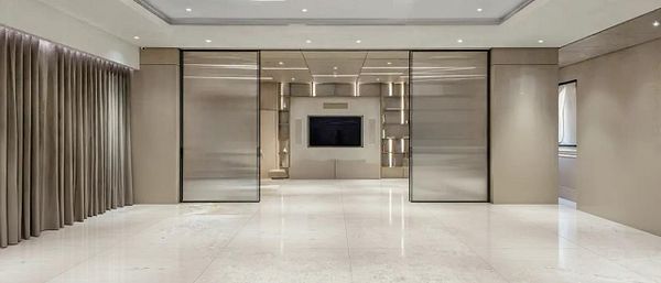 A spacious, modern living room with a minimalist design featuring large glass panels and neutral tones.