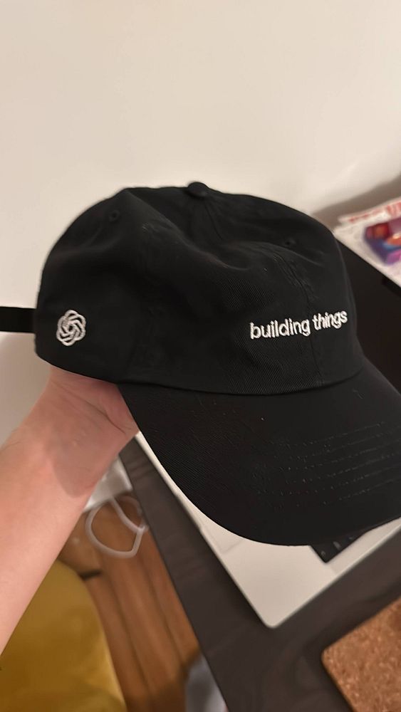 A photograph of a white baseball cap featuring the OpenAI logo on the front.