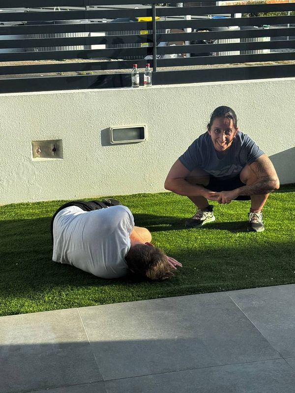 A personal trainer assists a client on a grassy area outside a hotel gym.