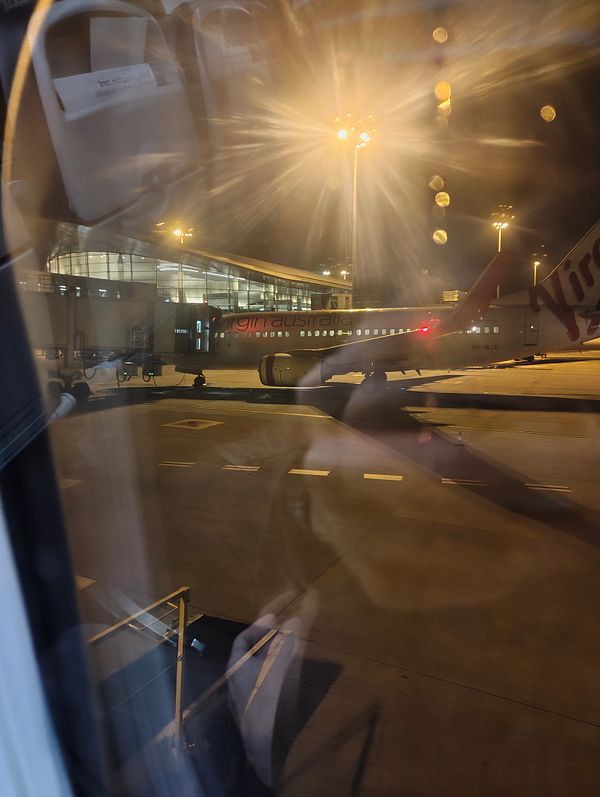 A view from inside an airport terminal showing a Virgin Australia plane on the tarmac at night.