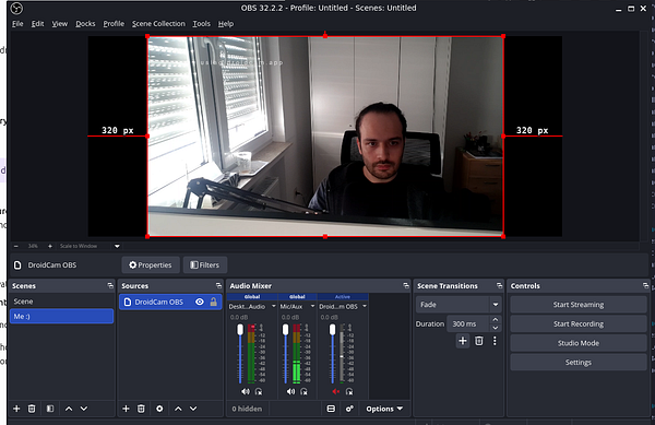 OBS Studio interface displaying a webcam feed of a person sitting in a room with natural light from a window, showing camera source settings and audio mixer levels.