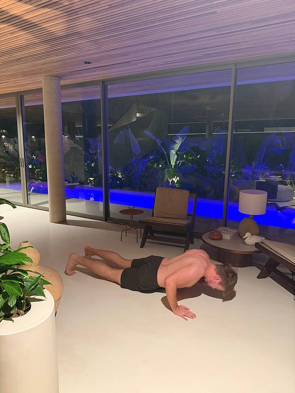 Woman performing a home workout exercise on a yoga mat in a bright room with tattooed arms and athletic attire.