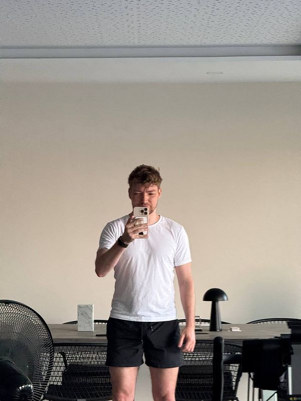 A person stands in front of a mirror, taking a selfie in a minimalistic room.