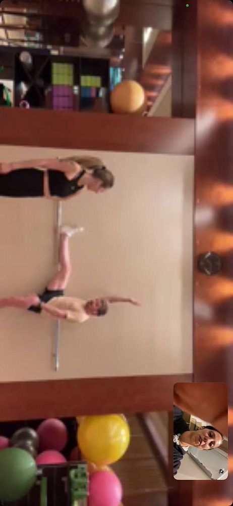 A gym scene featuring two individuals performing stretches with a barre.
