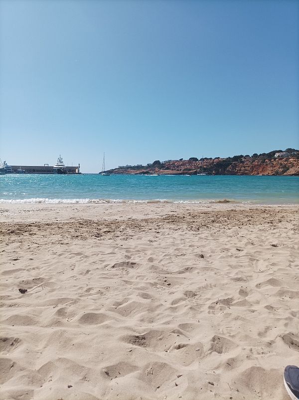 A serene beach scene on a hot day with clear blue water and a distant harbor.