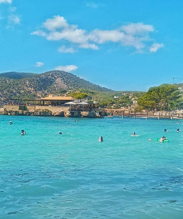 A vibrant beach scene with people swimming in clear turquoise water.