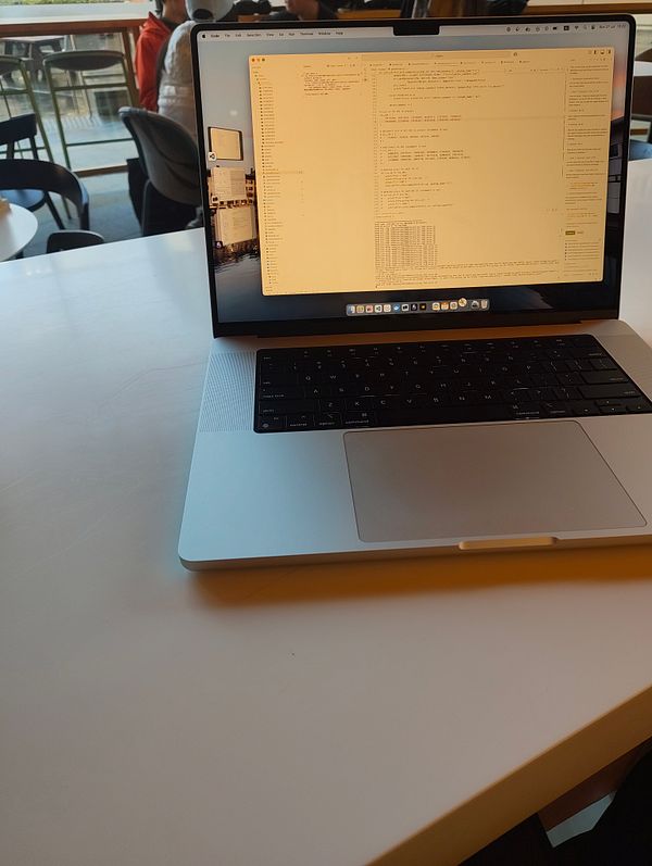 A laptop displaying code and data processing work is positioned on a table in a café setting.