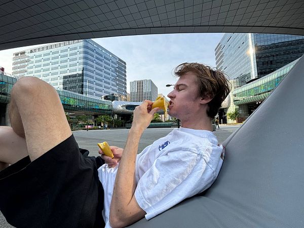 A young man relaxes on a bean bag outdoors, enjoying a snack in an urban setting.