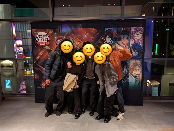A group of friends poses in front of a promotional backdrop for 'Demon Slayer: Infinity Castle' at an IMAX cinema.