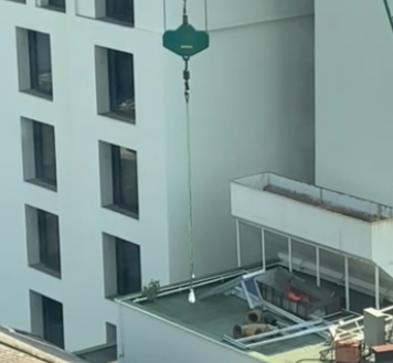 A construction crane is lifting a lunch container from a balcony.