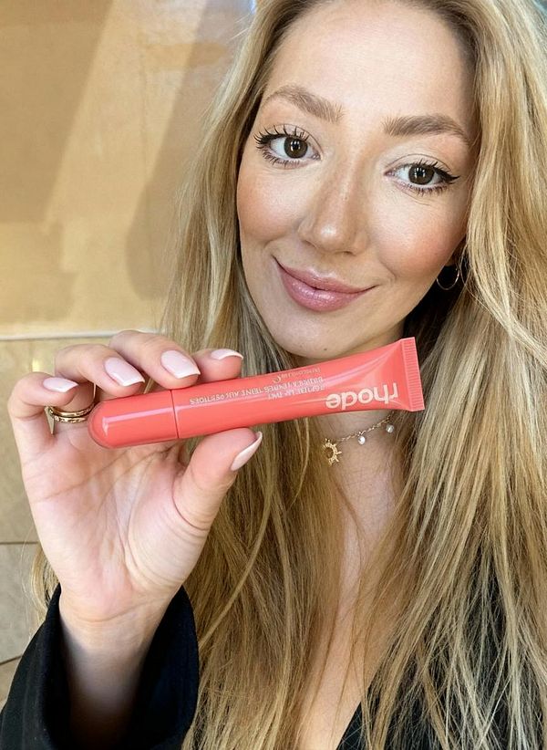 A woman holds a tube of product while smiling at the camera.