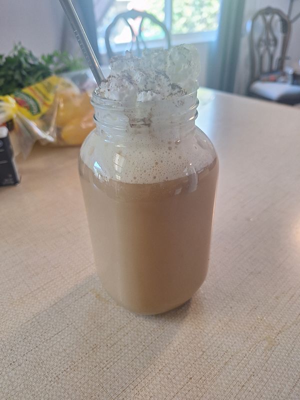A large jar filled with coffee topped with whipped cream and a sprinkle of cinnamon.