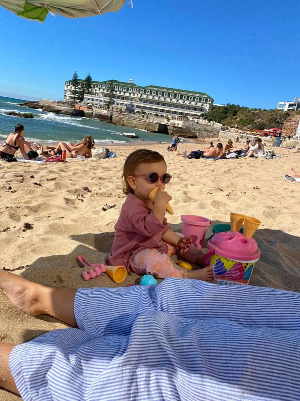 A young child enjoys a beach day with family, surrounded by toys and a scenic backdrop.