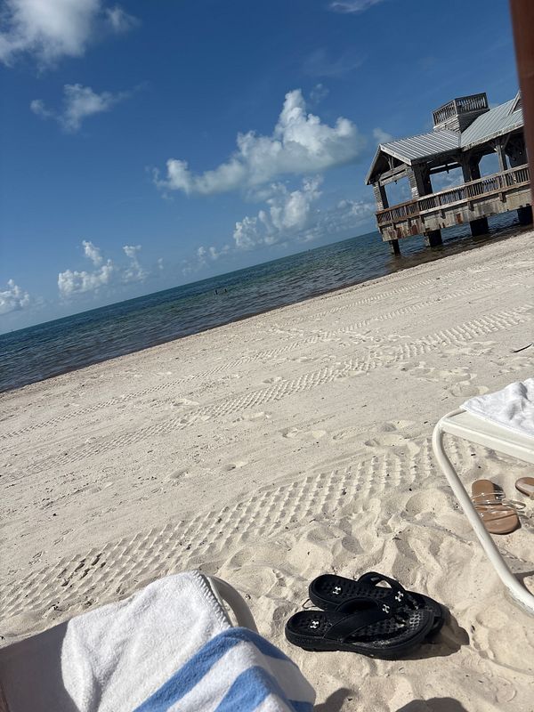 A serene beach scene in Key West featuring sand, water, and a wooden pier.