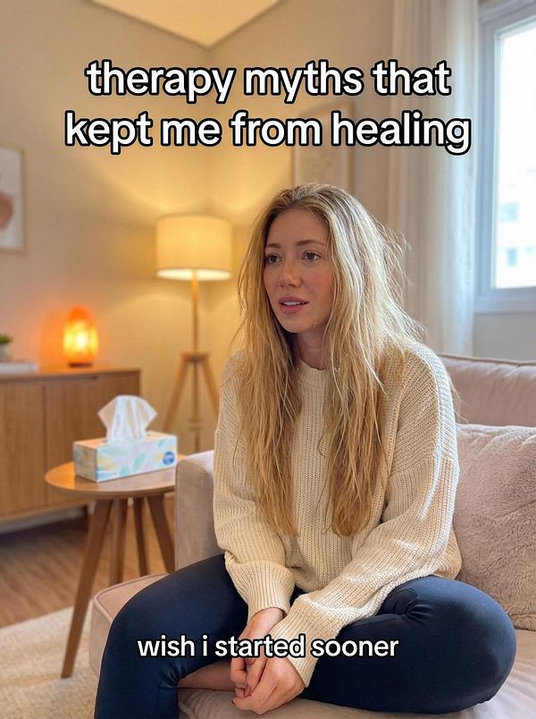 A young woman sits on a couch, reflecting on therapy myths that hindered her healing process.