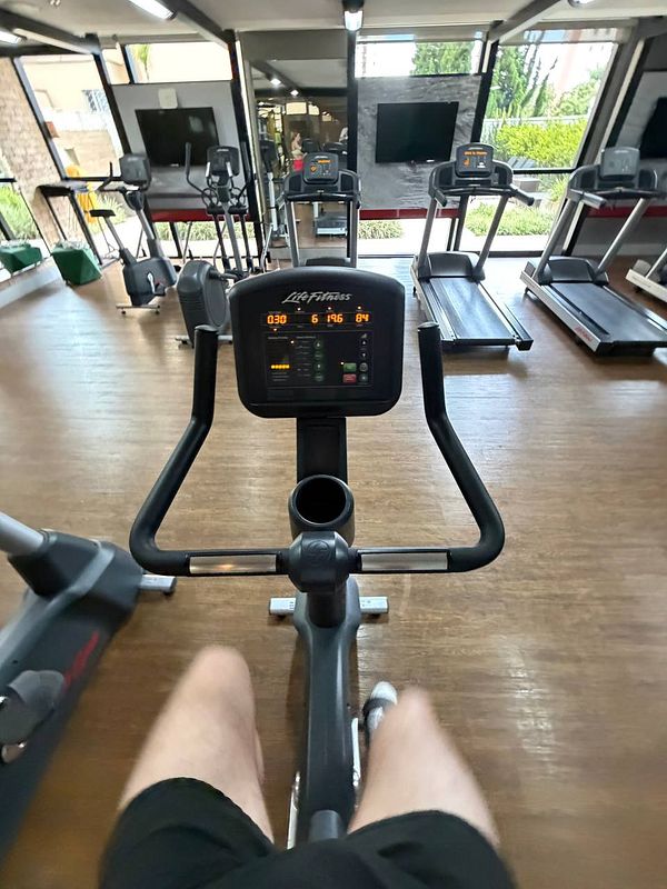 A gym setting featuring a man running on a treadmill while holding a tablet, likely for remote coaching, with exercise equipment visible around.