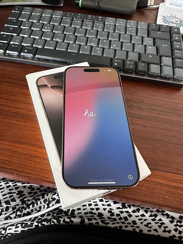 A new iPhone is displayed on a wooden desk alongside its box and a keyboard.