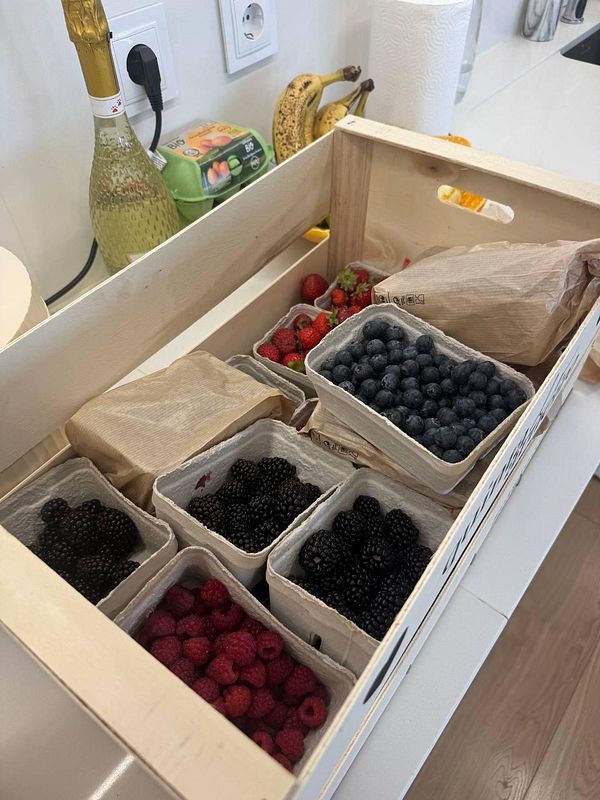 A wooden farm box filled with various types of berries and other items in a kitchen setting.